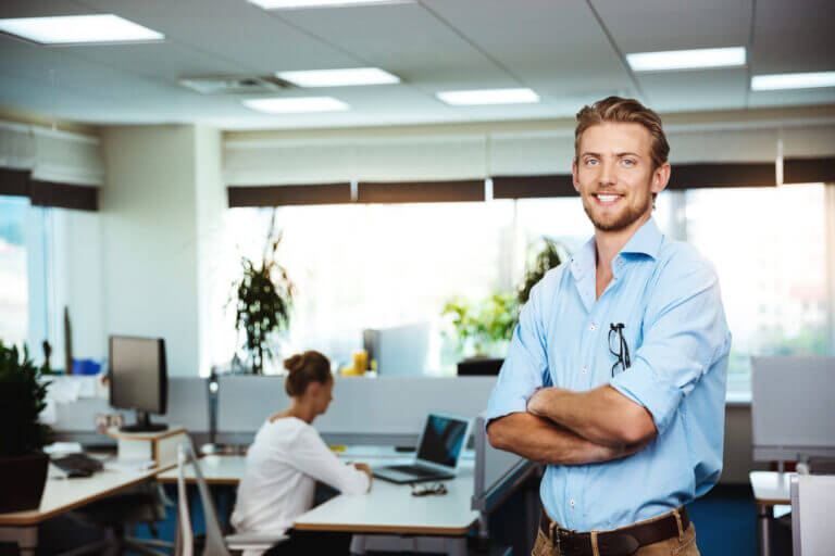 Young handsome successful businessman smiling, posing with crossed arms, office background.